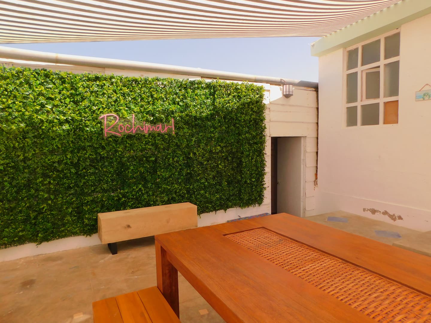 Patio de Rochimar con letrero de neón rosa sobre muro verde